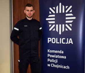 Policjant stoi przy banerze na którym jest napis Komenda Powiatowa Policji w Chojnicach