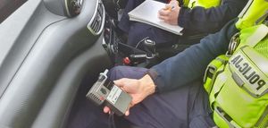 policjnt siedzący w radiowozie i tzrymający alkomat  w rękach