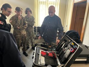 Grupa młodych ludzi w mundurach wojskowych przed nimi na stole leży otwarta walizka technika kryminalistyki