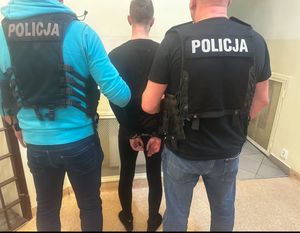 Policjanci kryminalni w policyjnych kamizelkach z napisem policja wraz z zatrzymanym