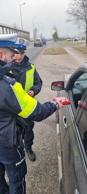 Dwóch policjantów stojących przy samochodzie przekazuje apteczkę