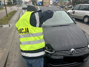 Policyjny technik wykonujący zdjęcia śladów na czarnym samochodzie osobowym stojącym na jezdni