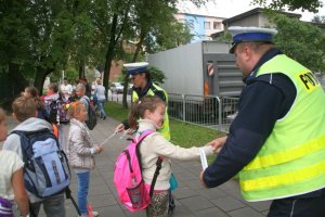 Policjant zakłada dziecku opaskę odblaskową