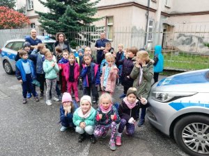 Grupowe zdjęcie dzieci z policjantami na tle radiowozu