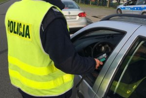 Policjant bada trzeźwosć kierującego. Policjant stoi przy pojeżdzie, kierowca siedzi w samochodzie