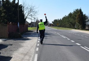 Policjant stoi na drodze z uniesiona tarczą do góry i zatrzymuje pojazd do kontroli