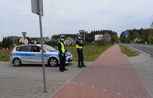 Policjanci stoja przed radiowozem. I czuwaja nad bezpieczeństwem rowerzystów