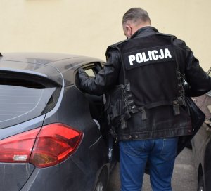 Policjant przy radiowozie w czasie doprowadzenia podejrzanego do auta