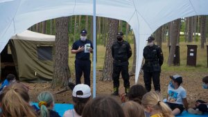 Policjant stoi przed harcerzami i prowadzi prelekcję