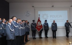 Policjnci stoją podczas uroczystości w szeregu, w tle widać  zaproszonych gosci