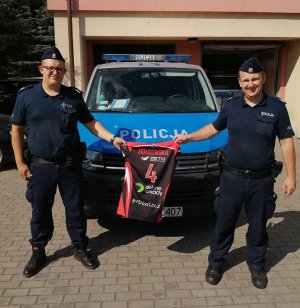 Policjanci trzymaja kozulke na licytacje na tle radiowozu