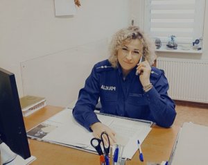 Policjantka siedzi za biurkiem i rozmawia przez telefon