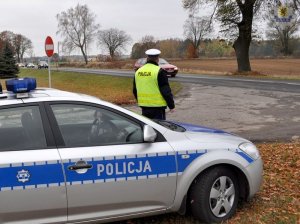 Policjant stoi przy radiowozie i obserwuje uczestnikw ruchu