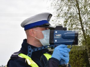 Policjant ruchu drogowego z maseczką na twarzy mierzy prędkość  predkościomierzem( zbliżenie)