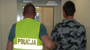 Policjant prowadzi podejrzanego- zarówno podejrzany jak i policjant widczni saod srony pleców