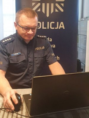 Policjant siedzi przy biurku przed laptopem.