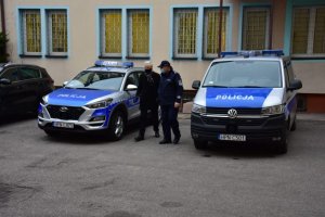 Policjant oglada wraz z mezczyzną nowe radiowozy- na zdjęciu są dwa pojazdy