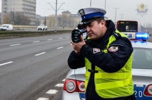 Policjant mierzy prędkość stojąc przy radiowozie