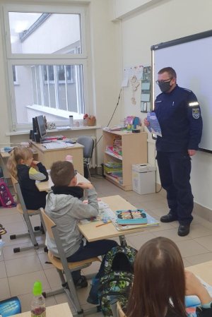 Policjant prowadzi pgadanke z uczniami w sali szkolnej stojąc przed nimi