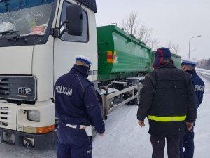 Dwaj policjanci i kierujacy stoja przy samochodzie ciężarowym