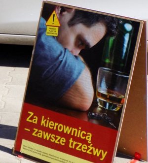 Plakat na którym przedstawiony jest mężczyzna pod wpływem alkoholu na nim widnieje napis- Za kierownicą zawsze trzeźwy