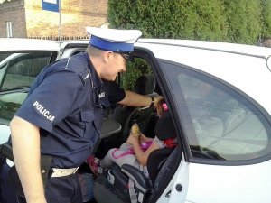 Policjant sprawdza prawidlowość zabezpieczenia dziecka w foteliku