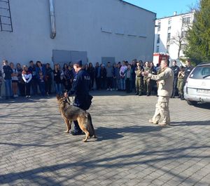 Na palcu policjant z psem oraz grupa młodziezy