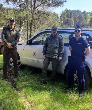 Policjant ze strażnikami leśnymi stoją przed pojazdem