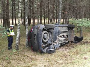 policjant piszący dokumentację przy przewróconym samochodzie w lesie