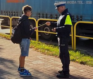 POLICJANT WRĘCZAJĄCY CHŁOPCU OPASKĘ ODBLASOWĄ