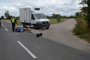 rozbity samochód stojący na poboczu, na drodze leży przewrócony motorower obok pracujący policjanci