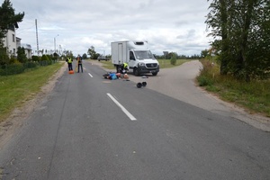 rozbity samochód stojący na poboczu, na drodze leży przewrócony motorower obok pracujący policjanci