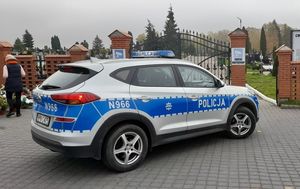 oznakowany radiowóz policji na tle bramy cmentarnej