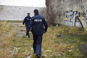 dwoje umundurowanych policjantów idących wzdłuż budynku pokrytego graffiti