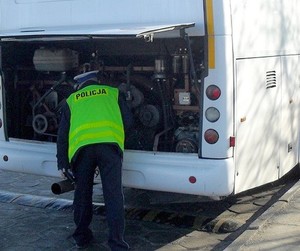 umundurowany policjant z kamizelce odblaskowej zaglądający do komory silnika autobusu