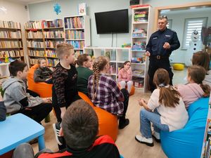 policjant stojący na środku pomieszczenia w bibliotece wokół siedzi grupka dzieci