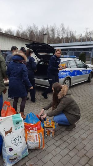 umundurowani policjanci oraz grupa cywili wypakowują karmę dla zwierząt z bagażnika oznakowanego radiowozu