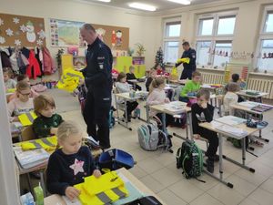 policjanci rozdający kamizelki odblaskowe dzieciom siedzącym w szkolnych ławkach