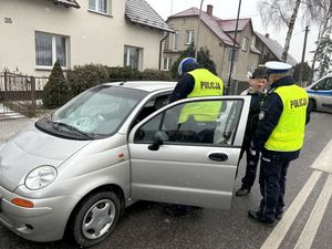 policjant w kamizelce odblaskowej stojący na jedni  przy rozbitym samochodzie