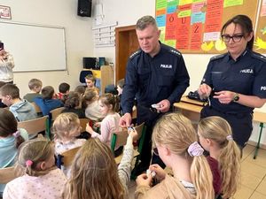 policjant i policjantka rozdający odblaski dzieciom