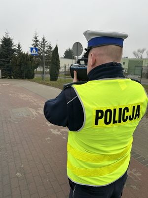 umundurowany policjant w żółtej kamizelce trzymający miernik prędkości