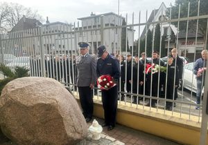 Policjanci stojący przed upamiętniającym obeliskiem z bukietem kwiatów w rękach