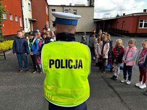 policjant w żółtej kamizelce z napisem policja stojący przed grupką dzieci