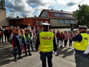 dwóch umundurowanych policjantów w żółtych kamizelkach przed grupą dzieci