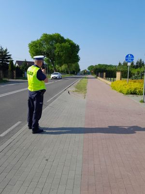 policjant stojący na chodniku mierzący prędkość nadjeżdżającego pojazdu