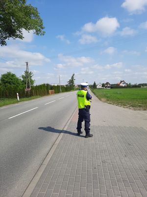 policjant stojący na chodniku mierzący  prędkość ręcznym miernikiem prędkości