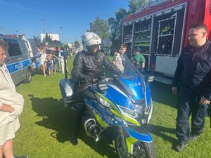 dziecko siedzące na policyjnym motocyklu, obok stoi policjant w służbowym kombinezonie