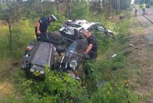 policjant stojący przy przewróconym motocyklu i rozbitym samochodzie w przydrożnym rowie