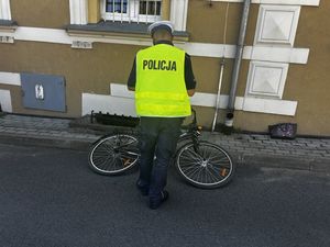 Policjant stojący przy opartym przed budynkiem rowerem