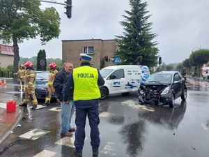 Umundurowany policjant stojący na jezdni, a w tle pojazdu biorące udział w kolizji